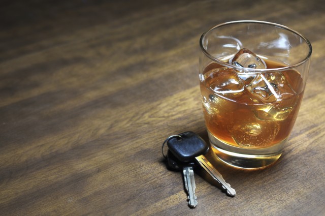 Glass of whiskey and car keys on wooden table.